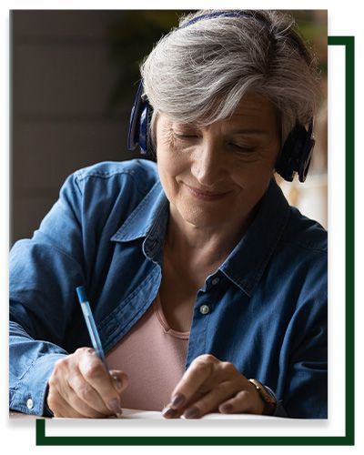 Woman with headphones writes on paper.