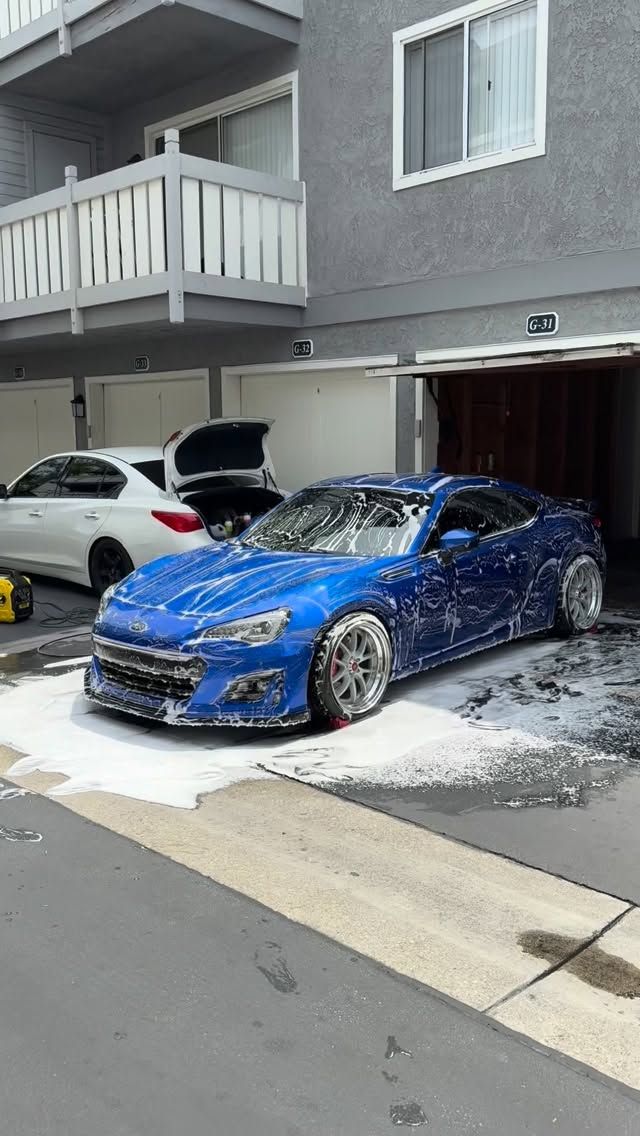 Blue sports car parked in a driveway with soap foam on the ground outside an apartment building