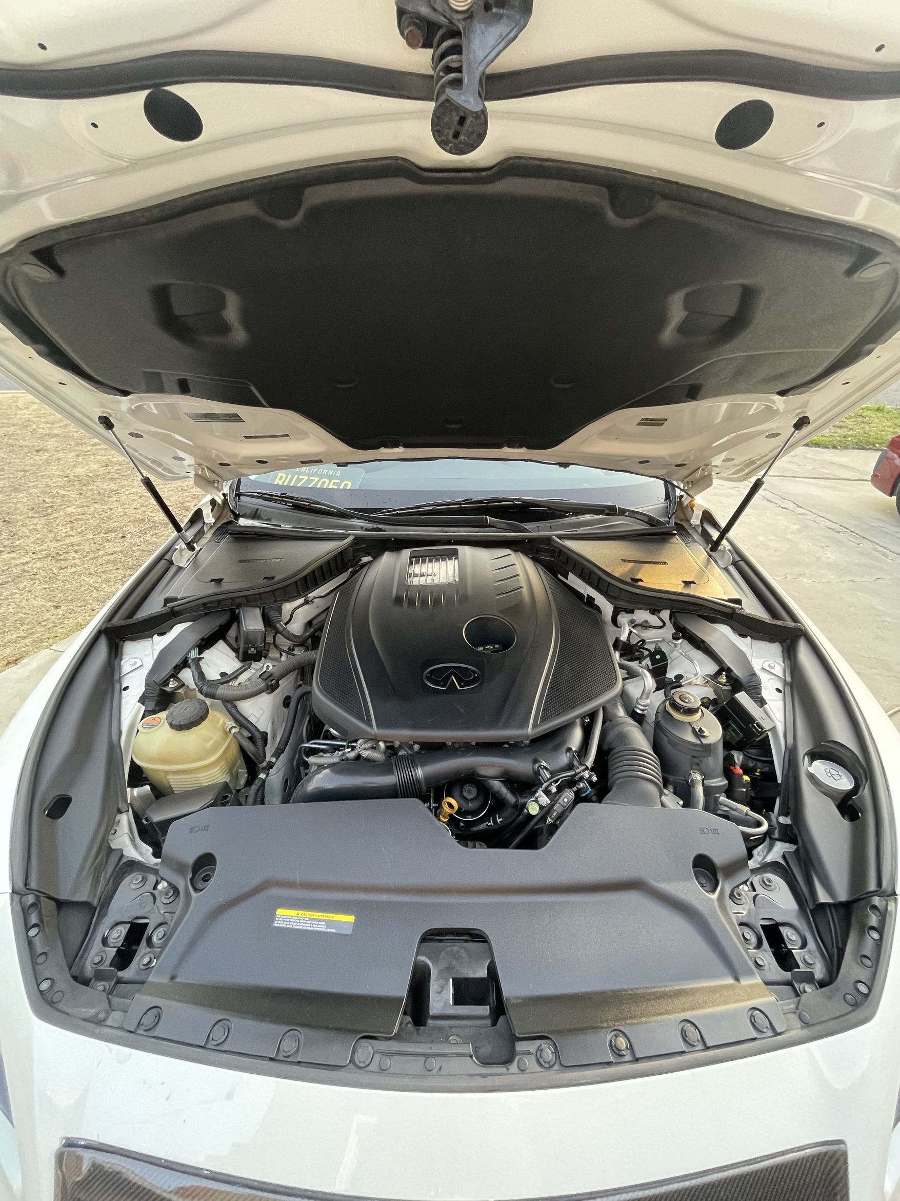 Open car hood showing an engine bay with a black engine cover and surrounding components