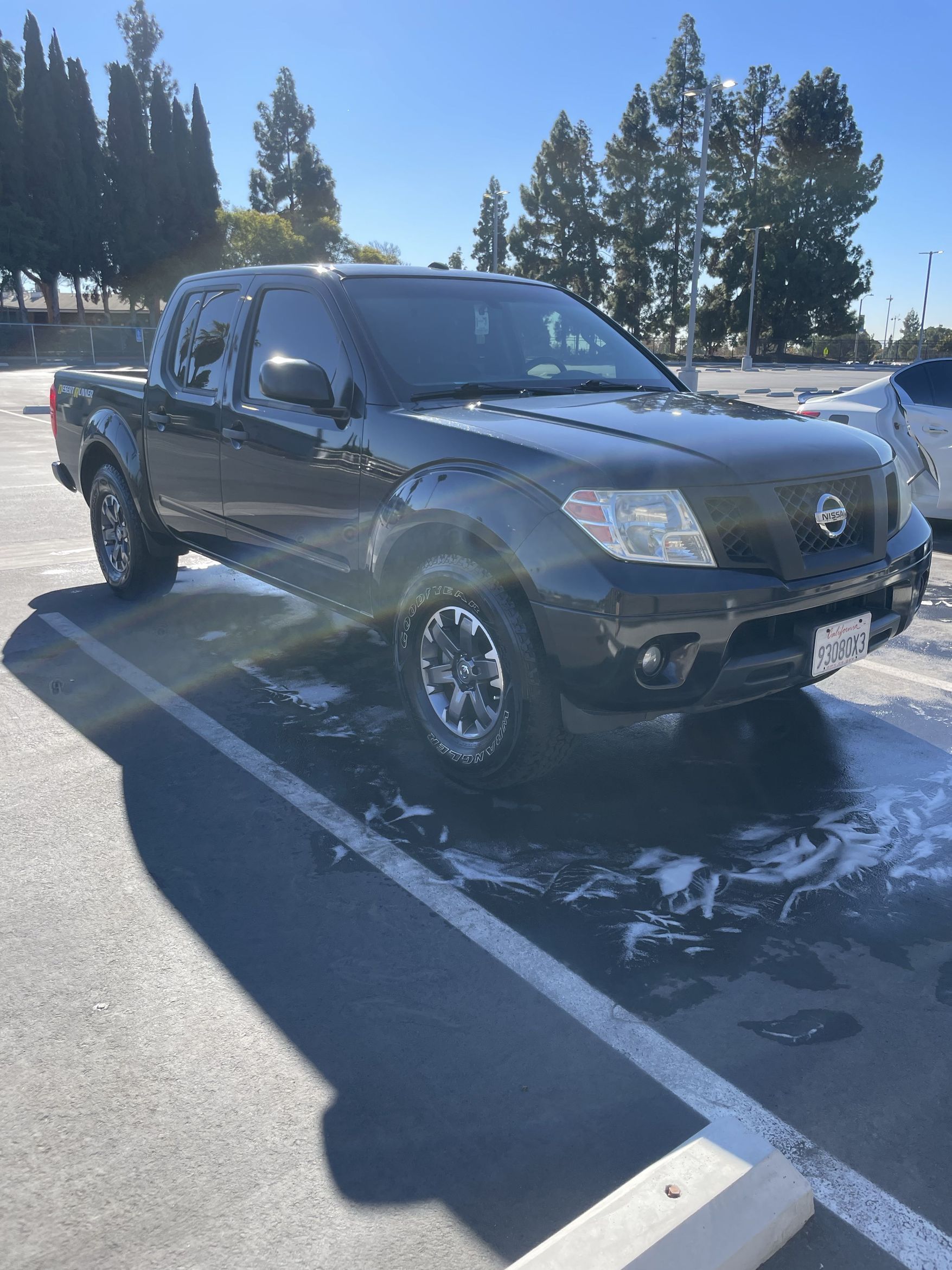 Dark gray pickup truck parked in a snowy lot with trees and bright sun in the background