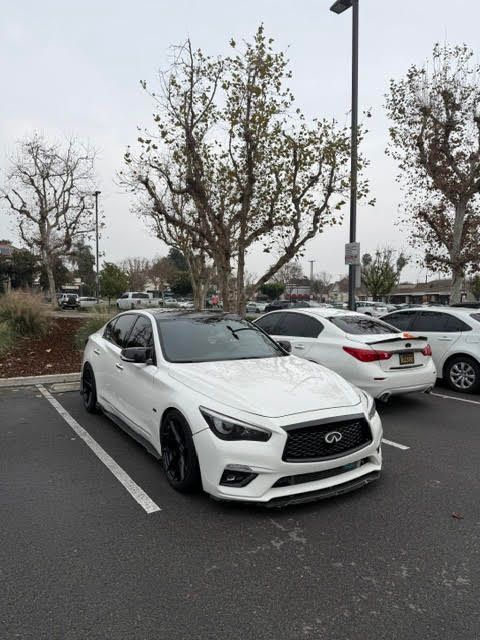 White sports car covered in foam, parked outdoors during a car wash.
