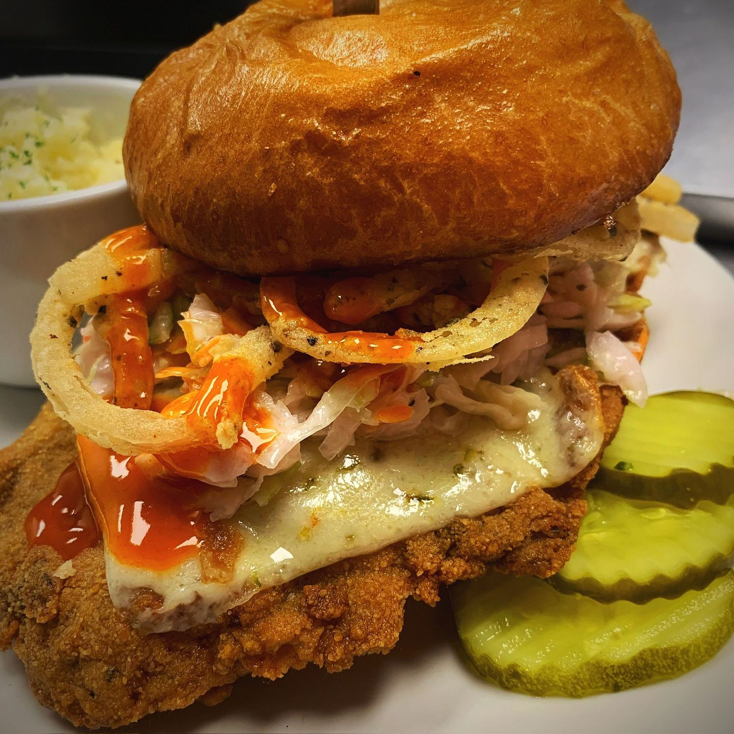 Chicken sandwich with toppings, onion rings, pickles, and mashed potatoes.