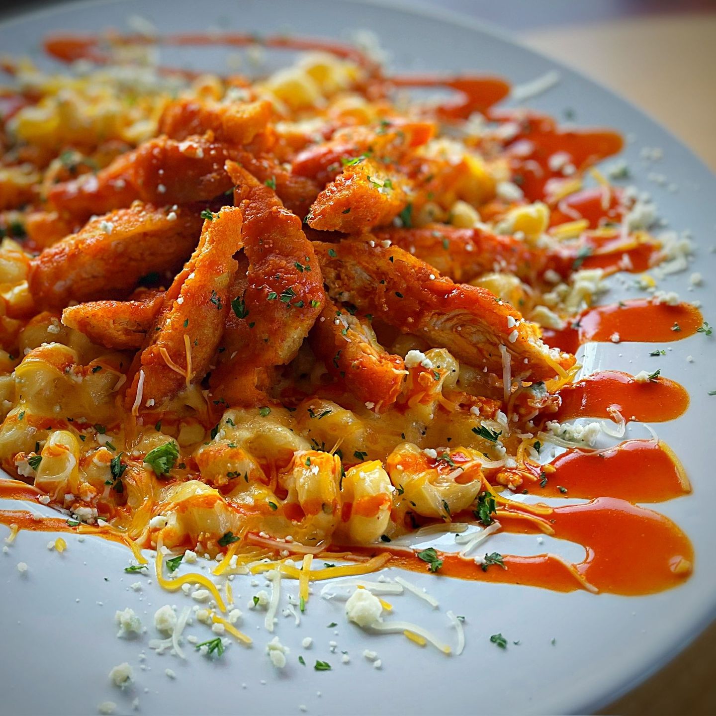 Mac and cheese topped with fried buffalo chicken, cheese, and sauce on a white plate.