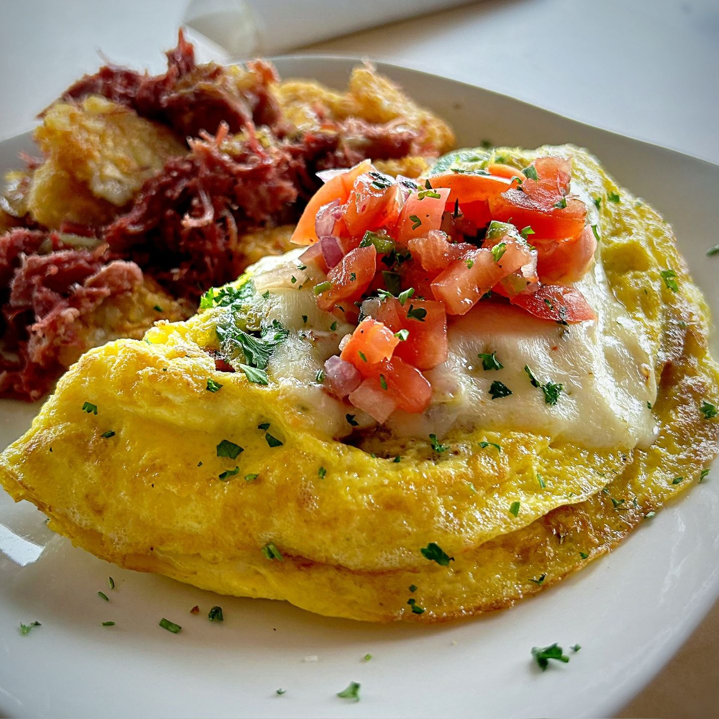 Omelet with white cheese and diced tomatoes, with corned beef and potatoes on a white plate.