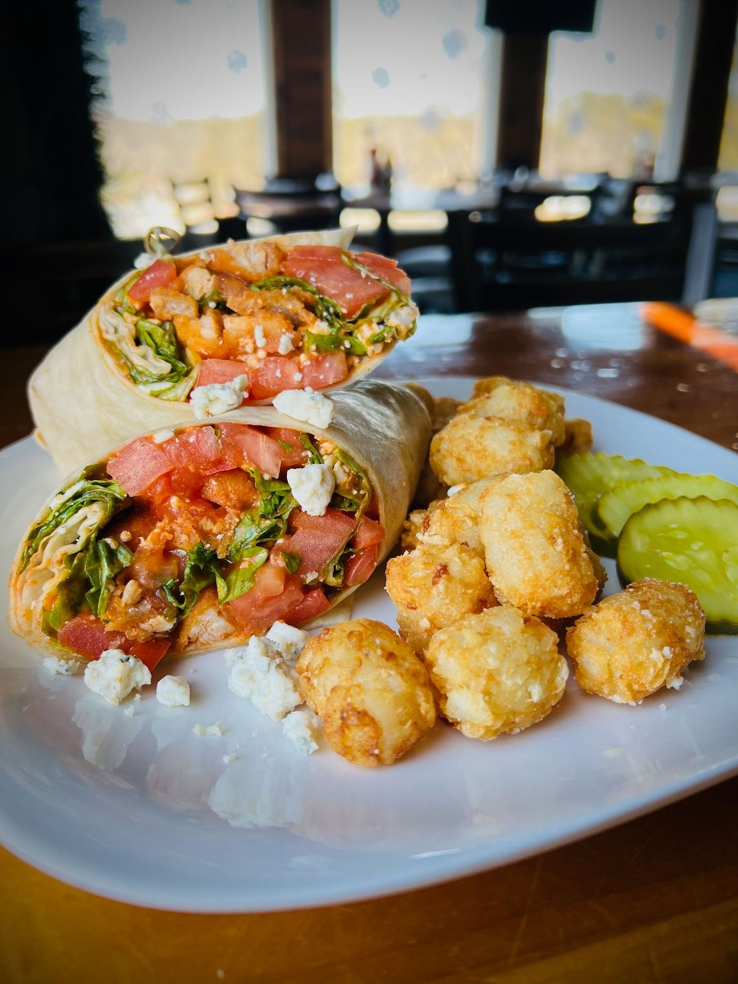 Wrap sandwich with tomatoes and lettuce, tater tots, and pickles on a plate.