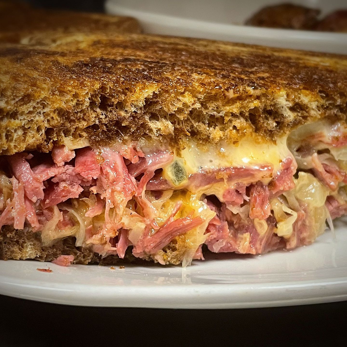 Grilled Reuben sandwich on a white plate; features corned beef, sauerkraut, and melted cheese between rye bread.