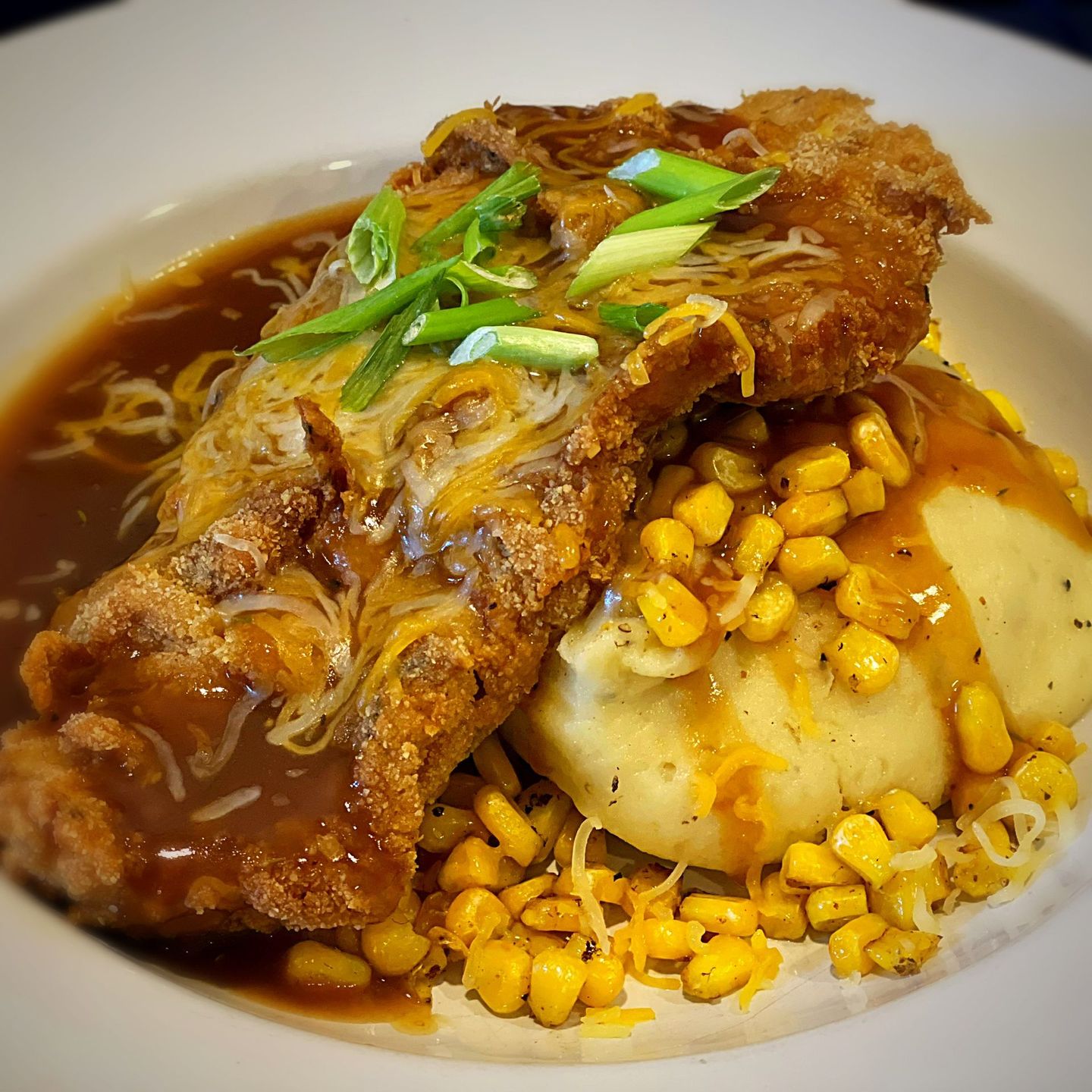Chicken fried steak with mashed potatoes, corn, gravy, and cheese.