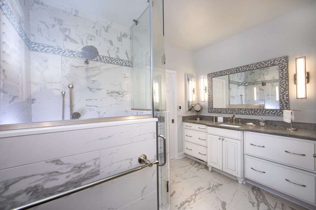 Bright white bathroom with glass shower, marble tub, and vanity with mirror and wall sconces