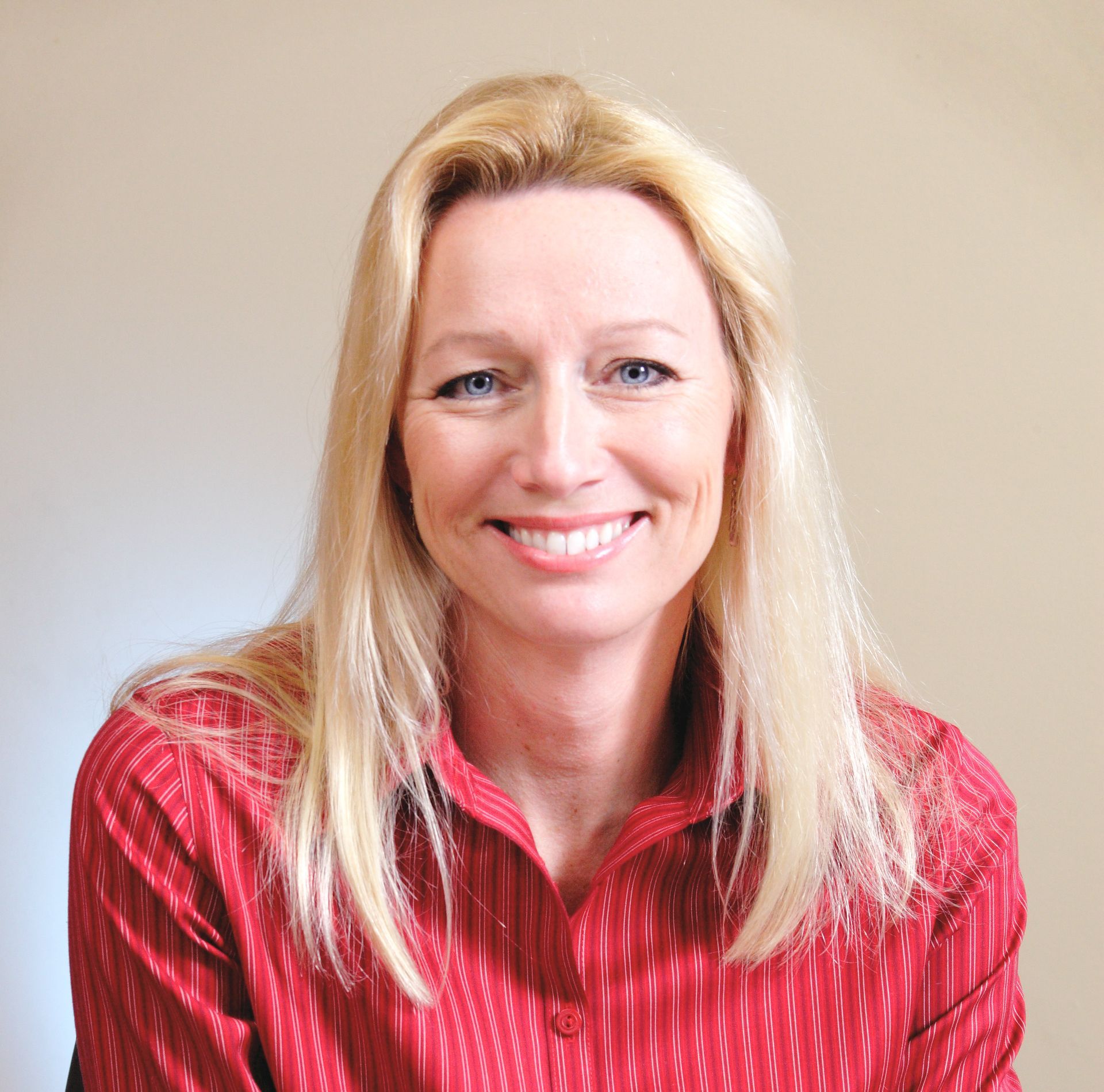 Smiling blonde woman in a red striped shirt against a plain beige background