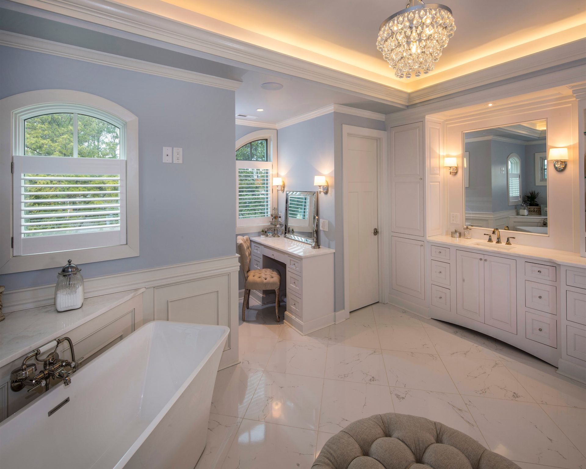 Bright marble bathroom with freestanding tub, double vanity, large mirror, and chandelier.