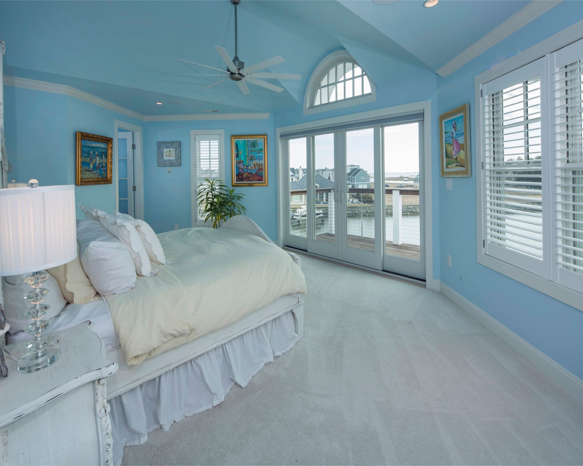 Light blue bedroom with white bed, vaulted ceiling, French doors, and ocean-view windows