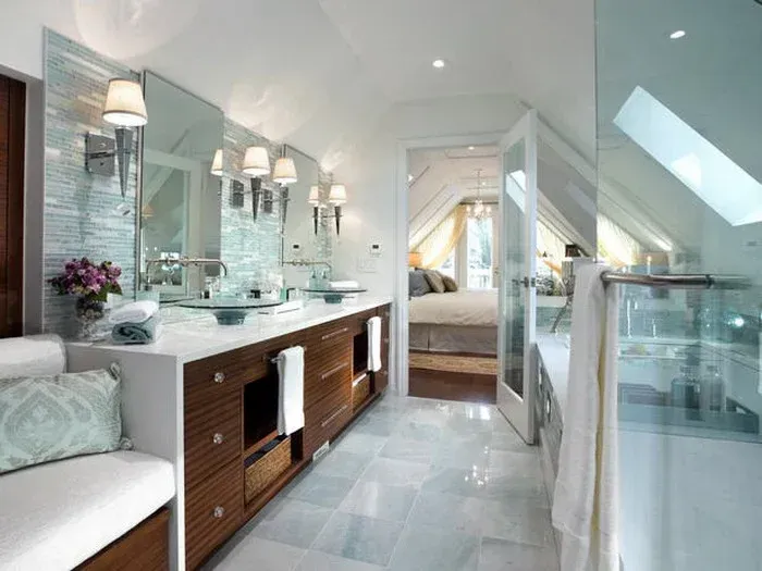 Bright modern bathroom with double vanity, glass shower, and skylight leading to a bedroom beyond