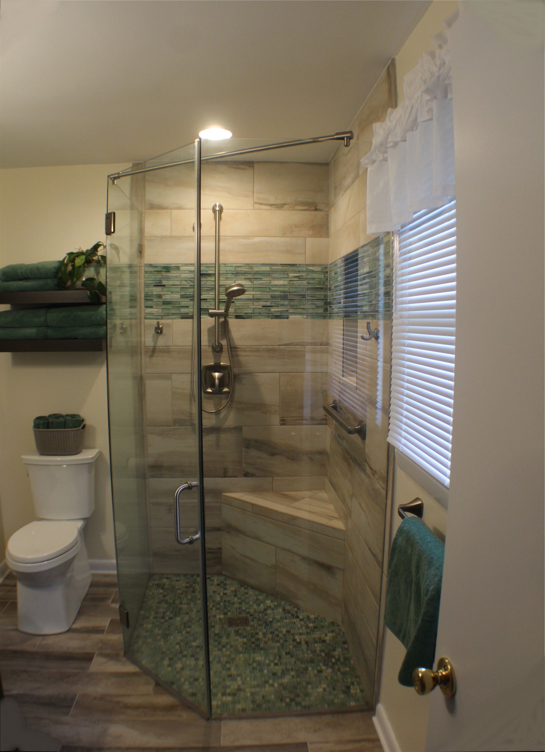 Walk-in shower with glass enclosure, stone tile floor, and a toilet beside it in a bathroom