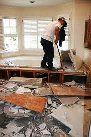 Man standing on debris inside a damaged room, removing flooring during renovation.