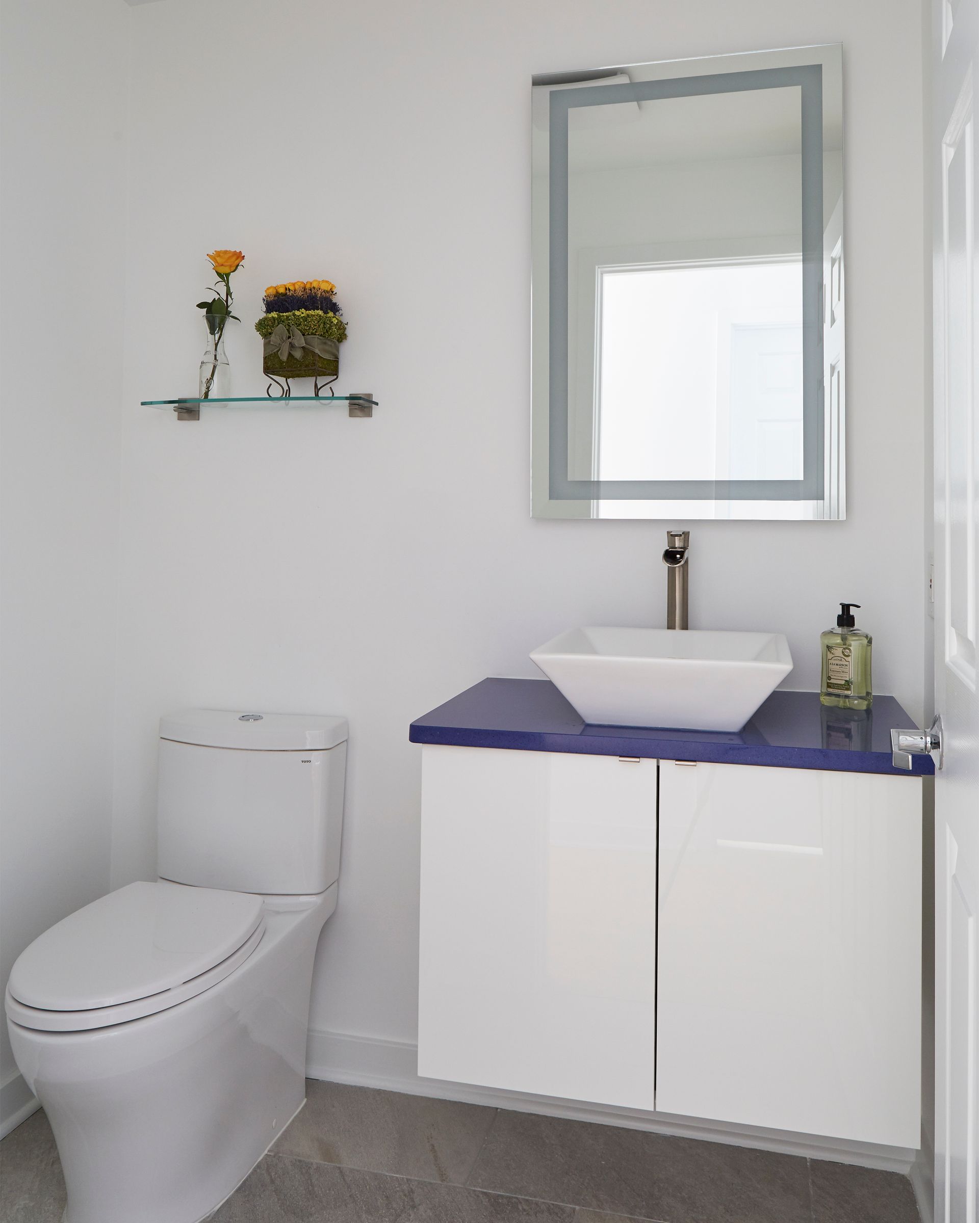 Modern bathroom with white toilet, purple vanity, sink, and wall mirror.