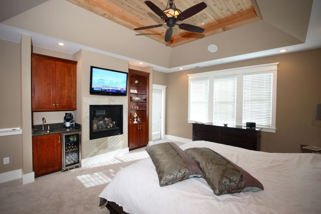 Bedroom with a bed, fireplace, wall TV, windows, and ceiling fan