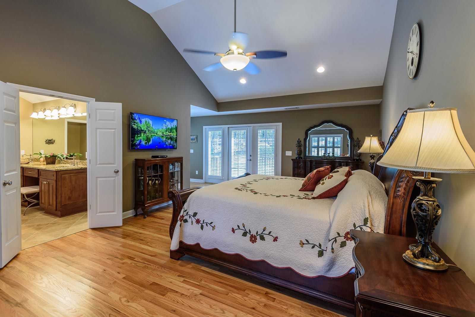 Spacious bedroom with a king bed, ceiling fan, TV, vanity, and open bathroom doorway