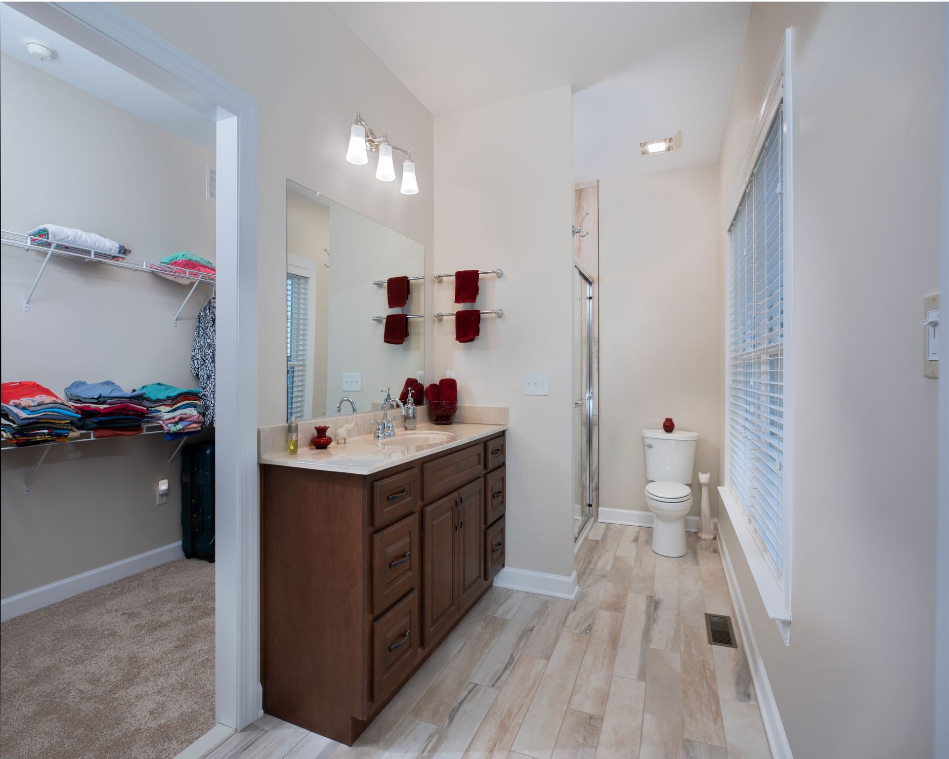 Bright bathroom with wood vanity, red towels, white tile floor, and a toilet in the back.