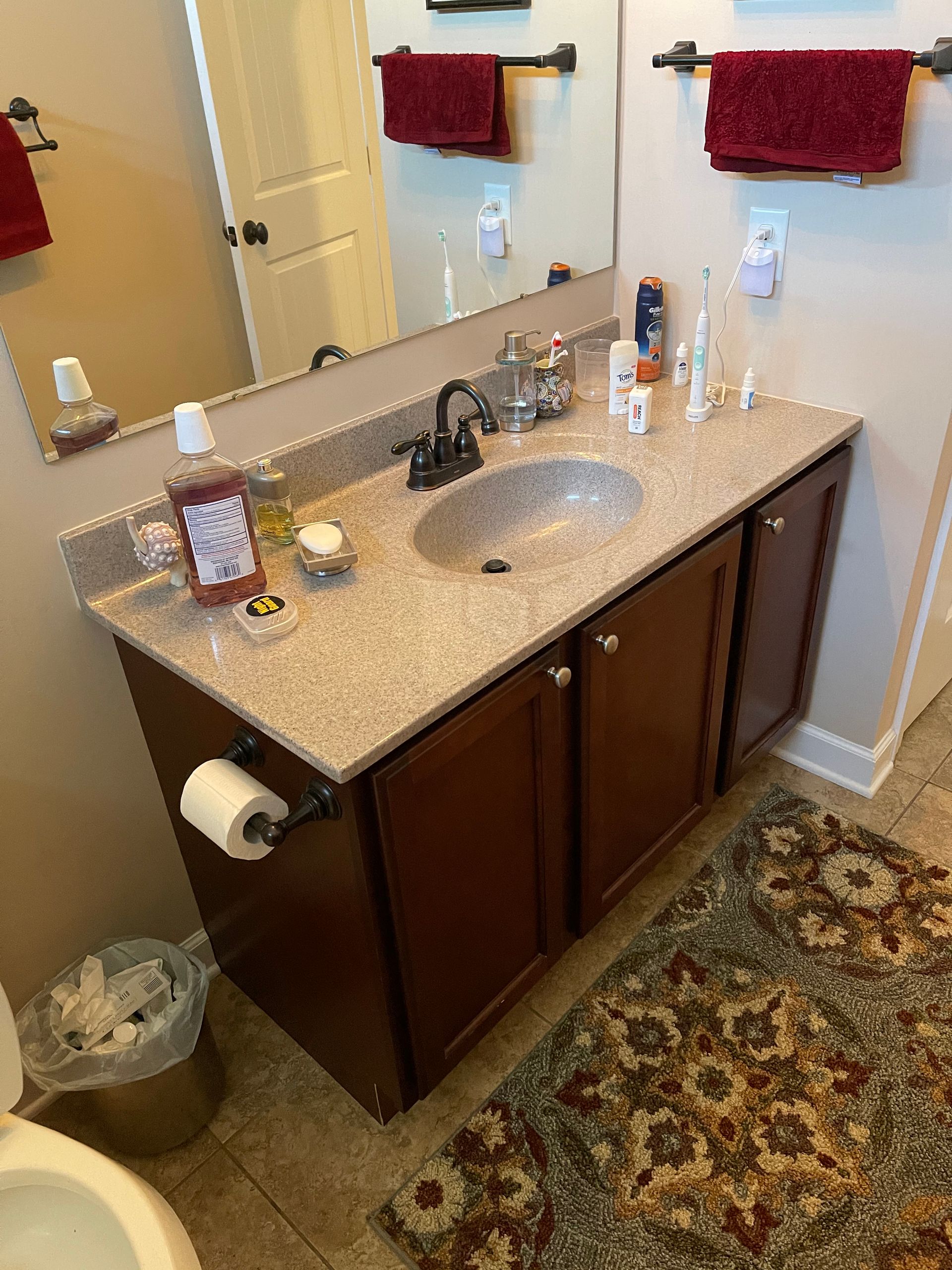 Bathroom vanity with sink, mirror, toiletries, and red towels above a dark wood cabinet.