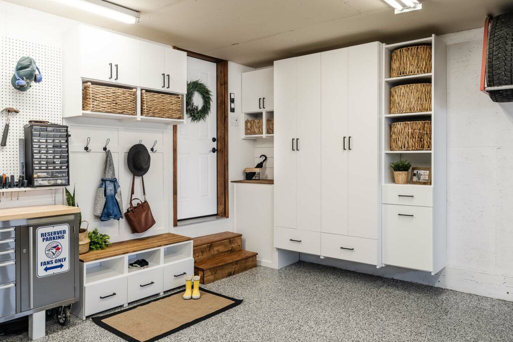Garage storage area with white cabinets, wall hooks, bins, and shelves of folded towels and supplies