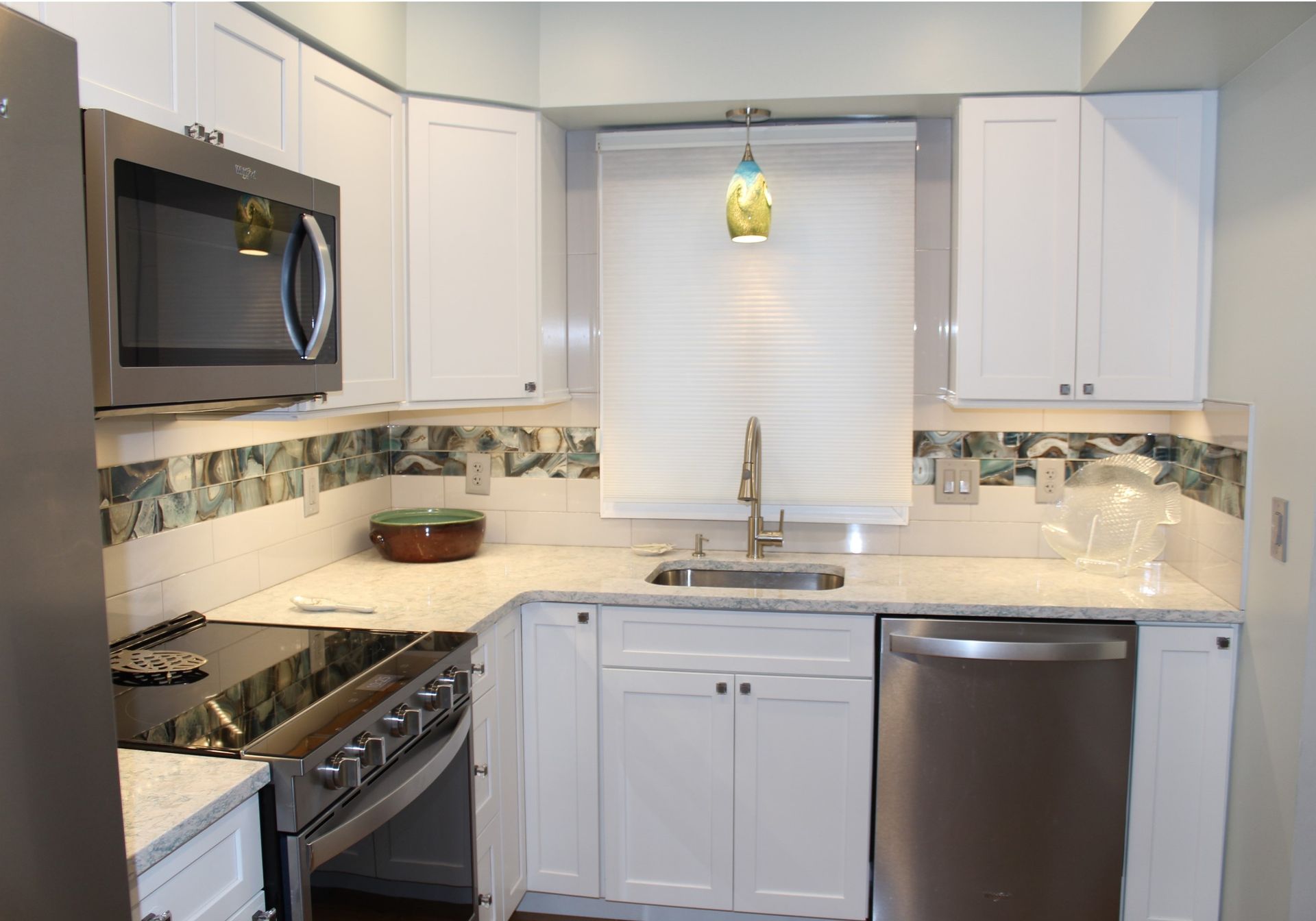 Modern white kitchen with stainless steel appliances, window over sink, and tiled backsplash