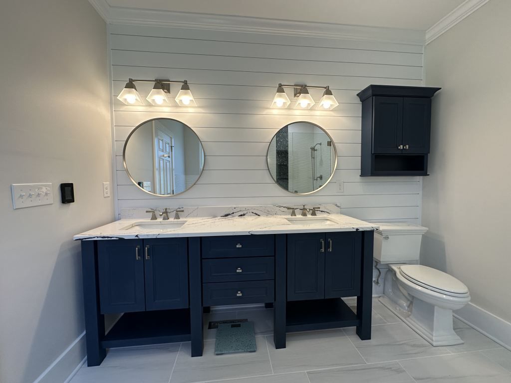 Bathroom vanity with navy cabinets, double round mirrors, and marble countertop under bright lights