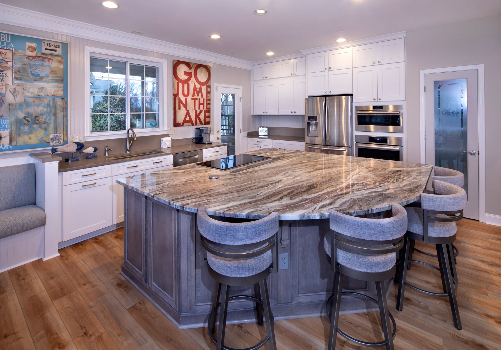 Bright modern kitchen with a large granite island, white cabinets, stainless appliances, and bar stools