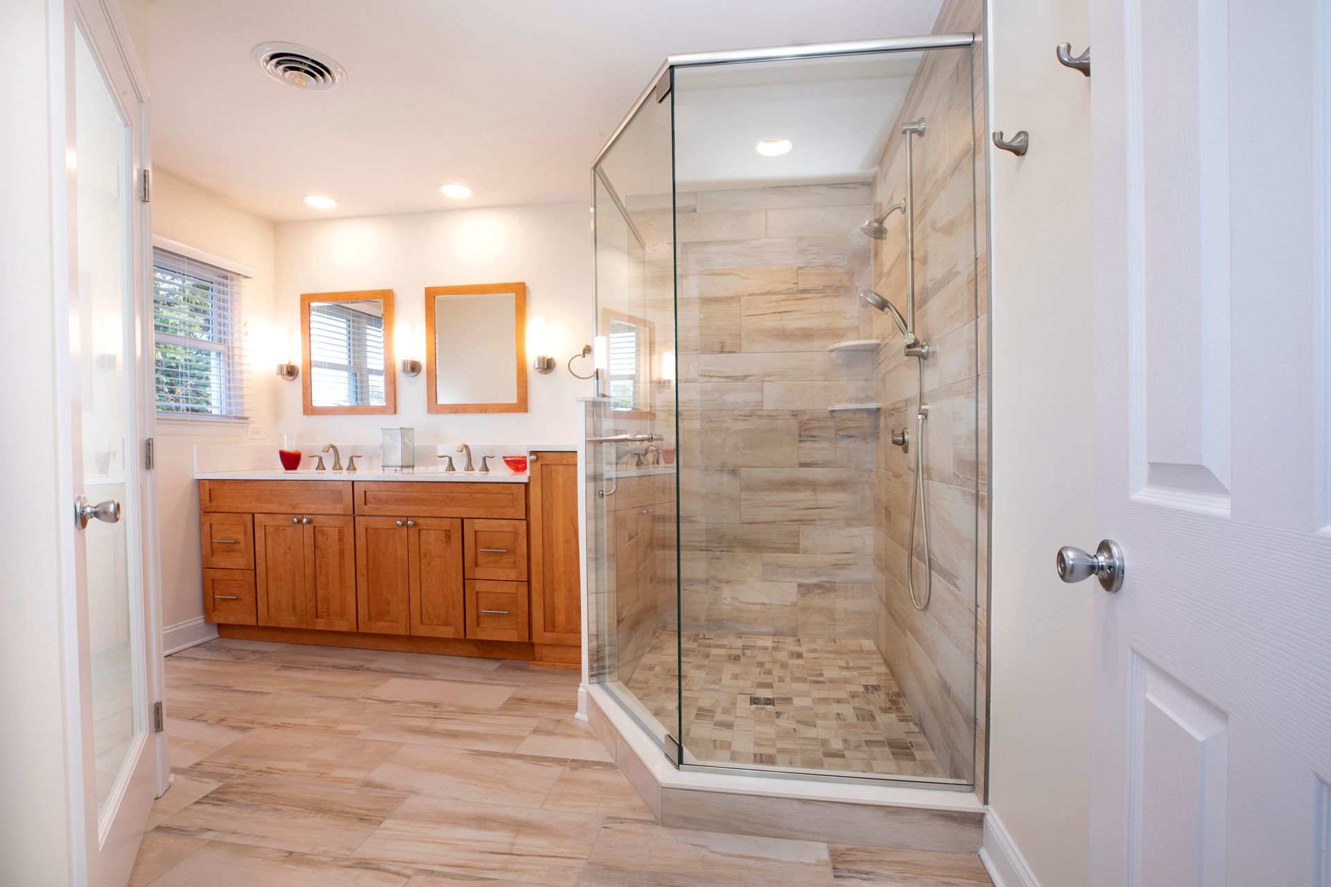Modern bathroom with double vanity, mirrors, and glass-enclosed shower on wood-look tile floor