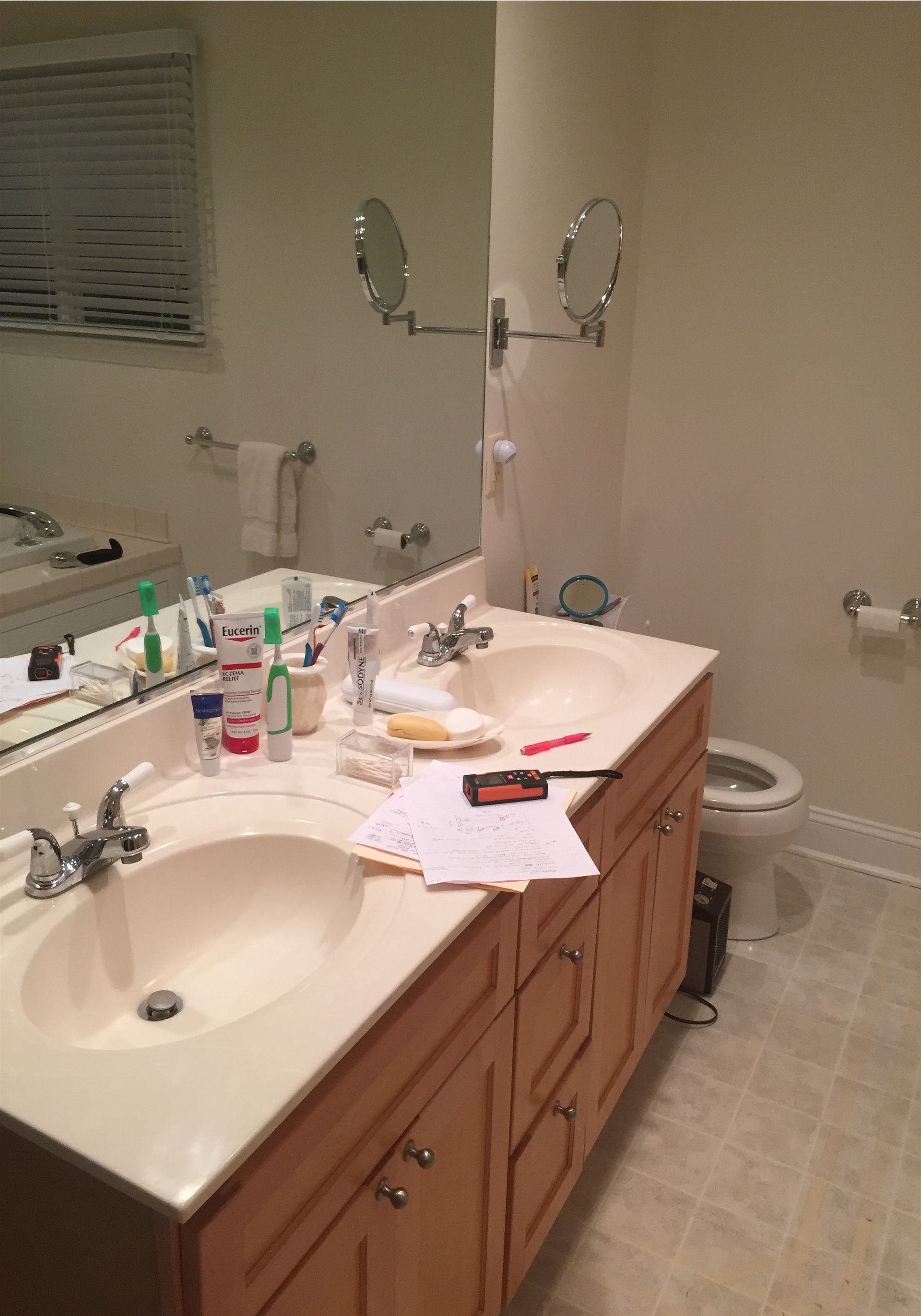 Cluttered bathroom vanity with sink, mirror, toiletries, papers, and a cluttered countertop.