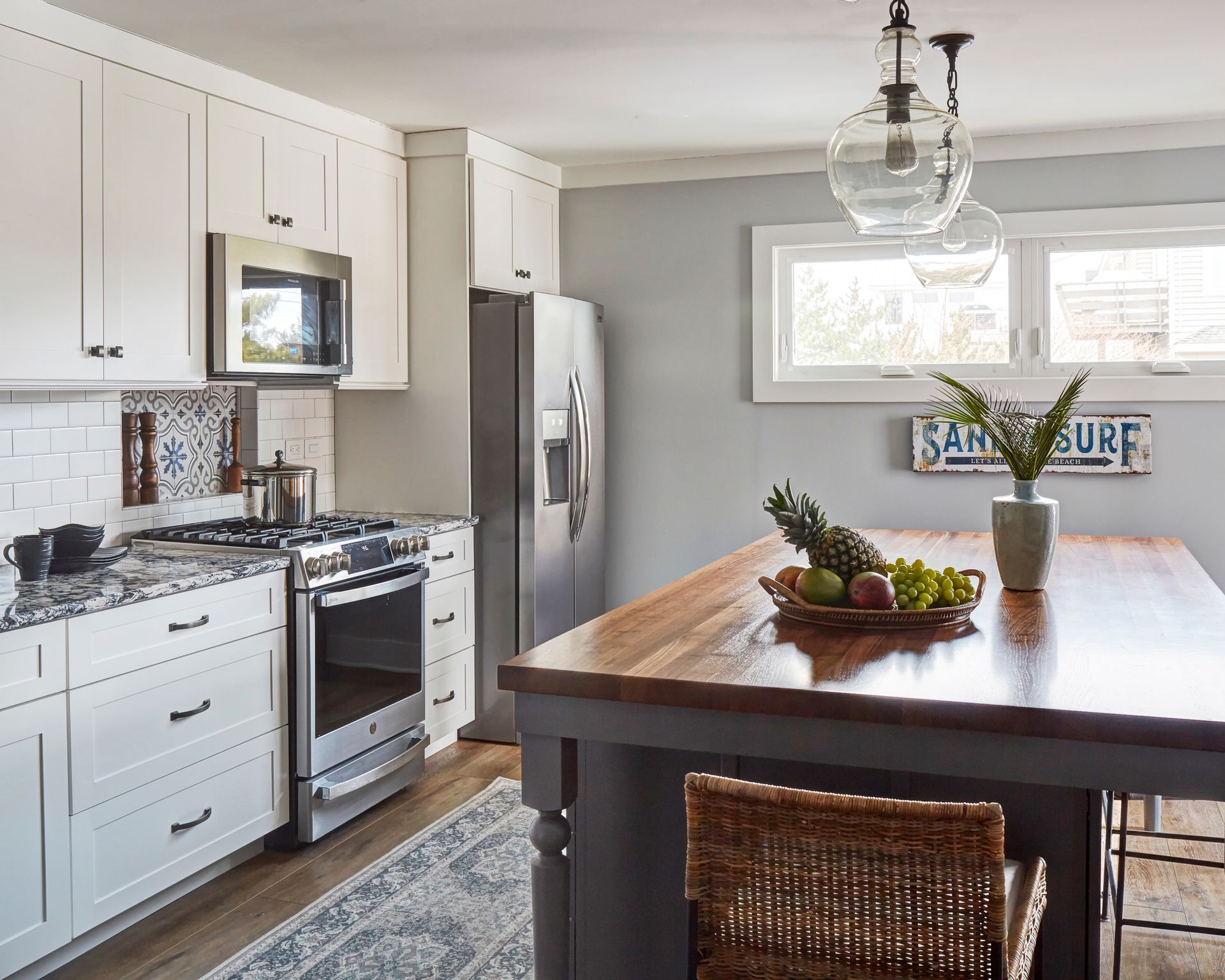 Bright kitchen with white cabinets, stainless stove and fridge, and a wood island with a fruit bowl and decor