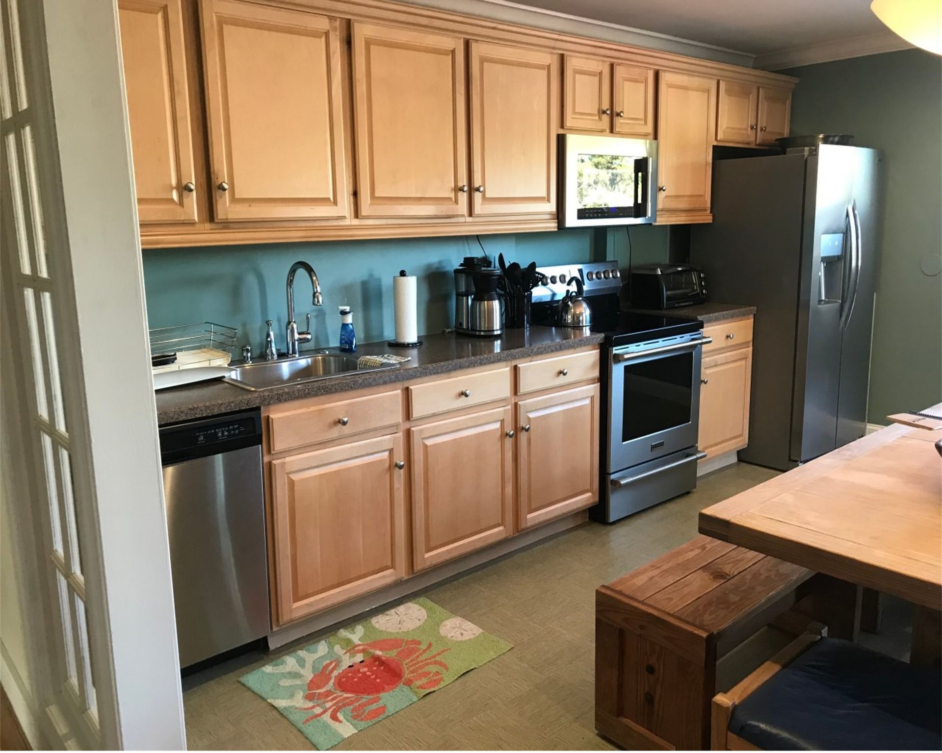 Bright kitchen with light wood cabinets, stainless fridge and stove, black countertops, and a wooden table in foreground