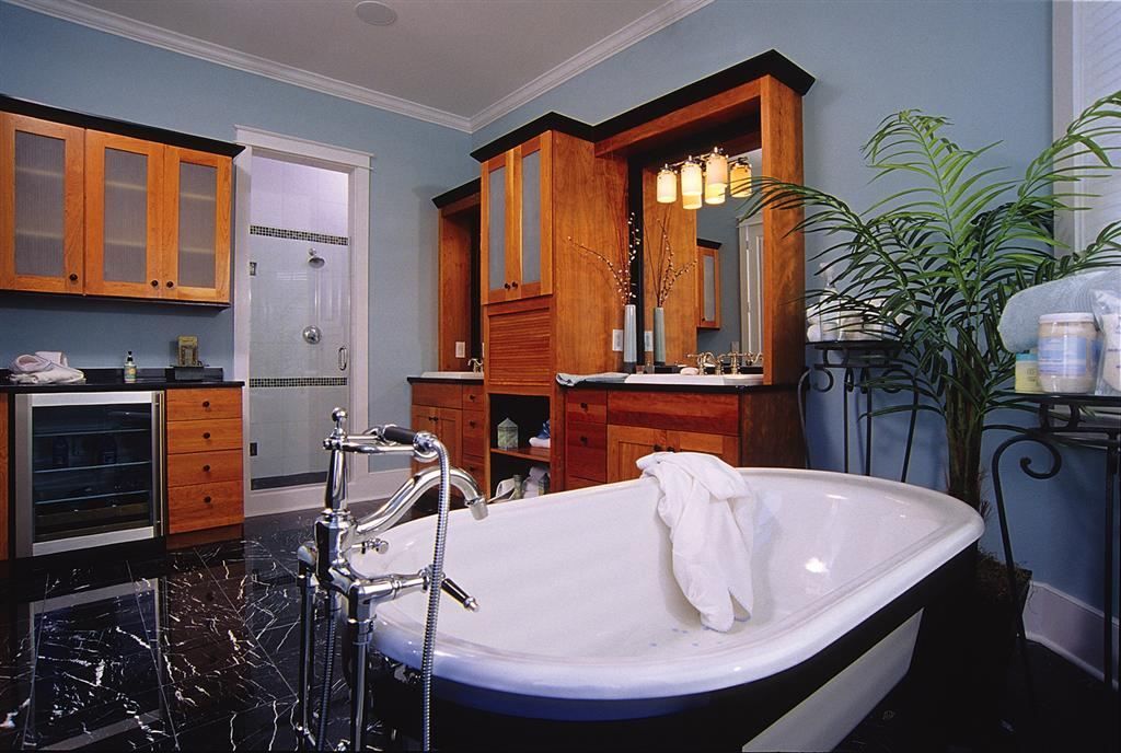 Bathroom with a white clawfoot tub, wooden cabinets, and a potted plant near a vanity mirror.