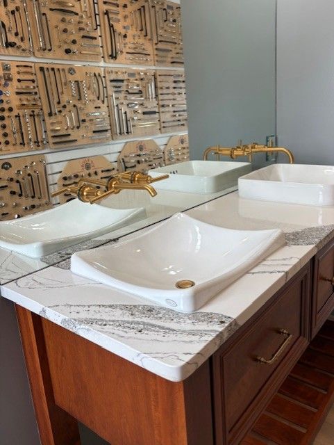 Bathroom vanity with two white vessel sinks and gold faucets against a patterned tile wall