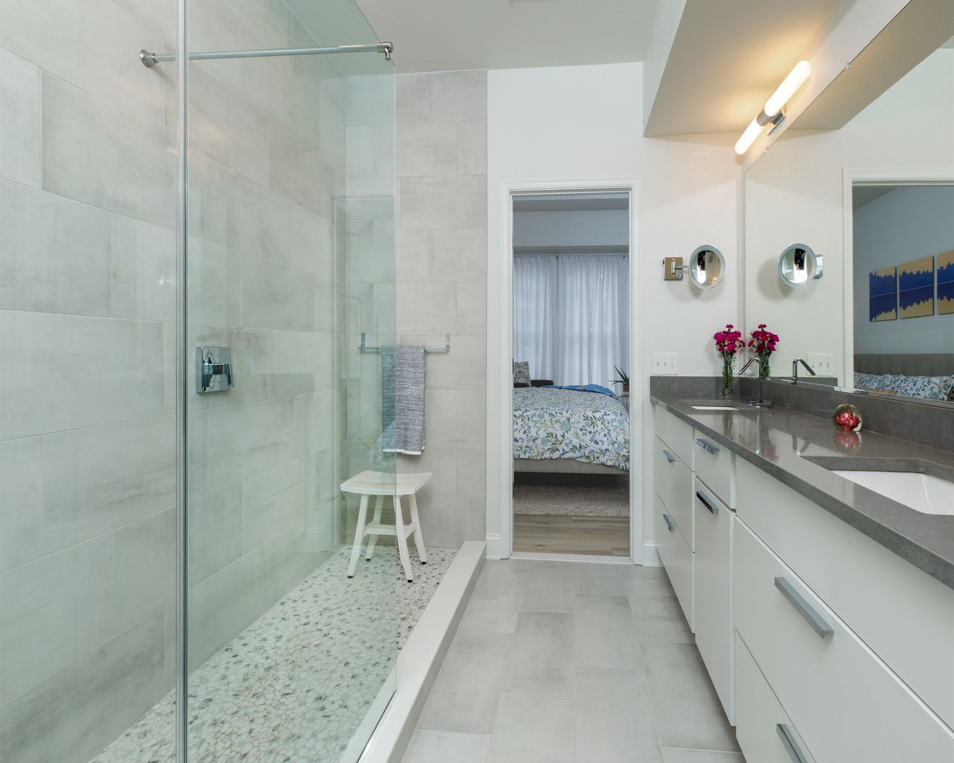 Modern white bathroom with glass shower, double vanity, and doorway to a bedroom