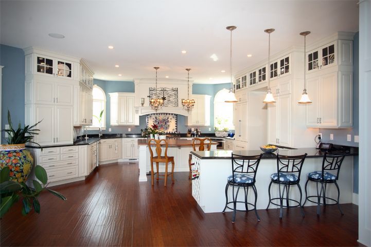 Bright kitchen with white cabinets, dark wood floors, island seating, and pendant lights