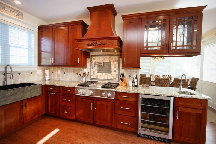 Wooden kitchen with granite counters, tiled backsplash, and stainless-steel oven under a range hood