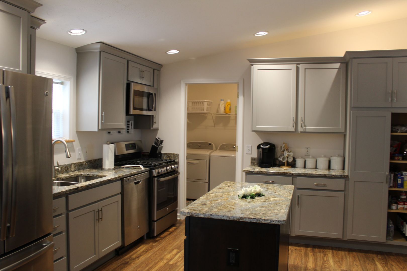Modern kitchen with stainless steel appliances, gray cabinets, and a granite island under recessed lights