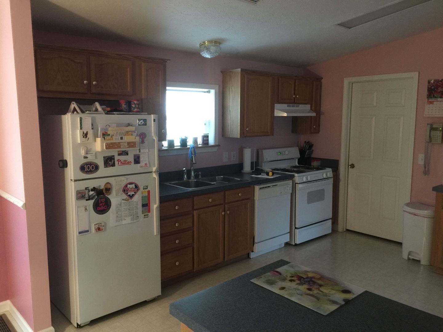 Small kitchen with wooden cabinets, white appliances, and a window over the sink.