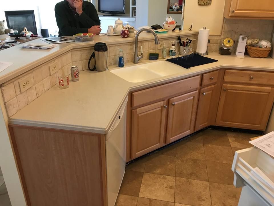 Kitchen counter and sink with beige cabinets and a person standing in the background.