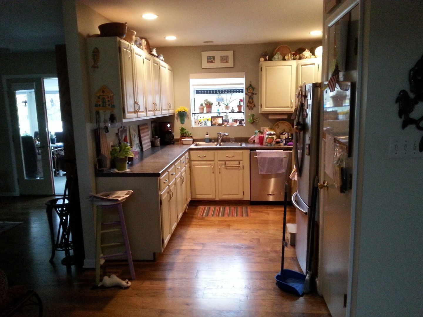 Narrow kitchen with cream cabinets, wood floors, and warm overhead lighting, seen from a doorway.