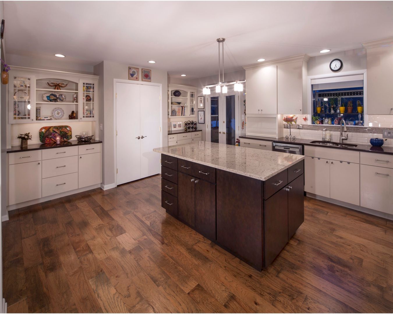 Modern kitchen with dark island, white cabinets, hardwood floor, and pendant lights