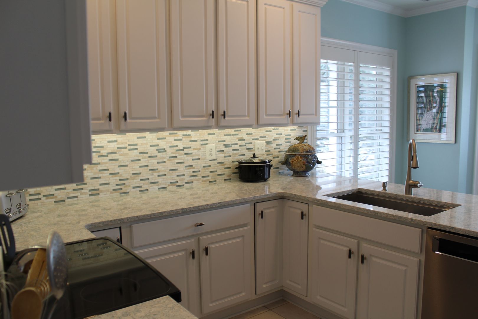 Bright kitchen with white cabinets, mosaic backsplash, and a sink by a window.