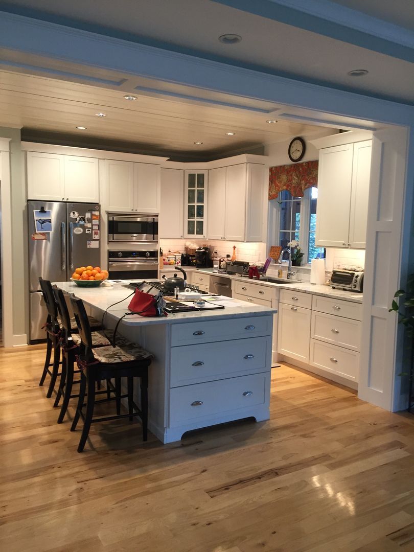 Bright white kitchen with island, bar stools, stainless steel refrigerator, and hardwood floors