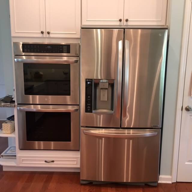 Stainless steel refrigerator beside a double wall oven in a white kitchen