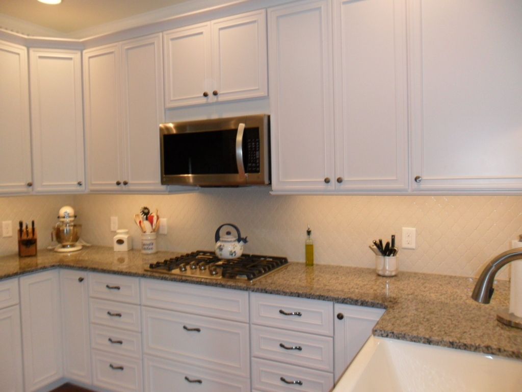 White kitchen with granite countertops, white cabinets, microwave, stove, and utensils on the counter