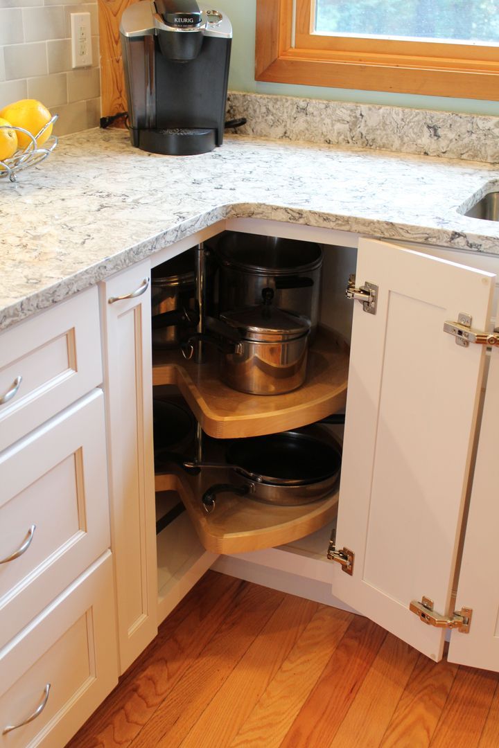 Open kitchen corner cabinet with a pull-out shelf and stacked cookware beneath a countertop.
