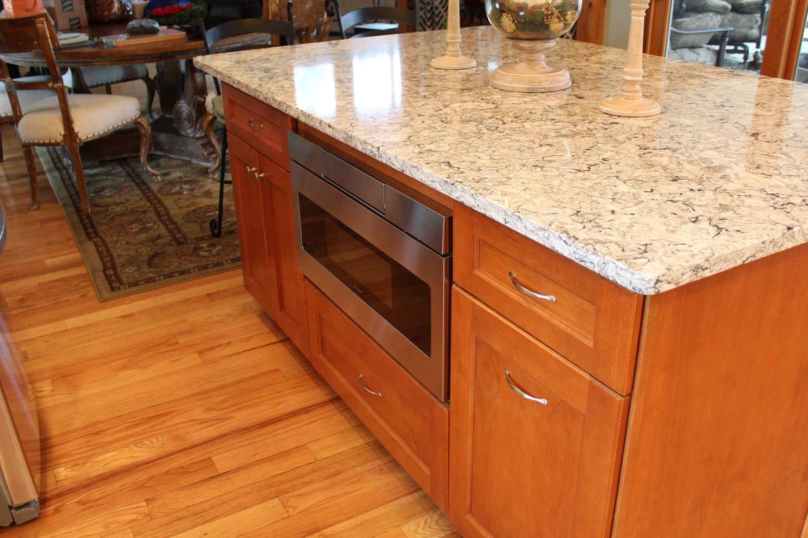Kitchen island with granite countertop, wood cabinets, and built-in microwave on a hardwood floor