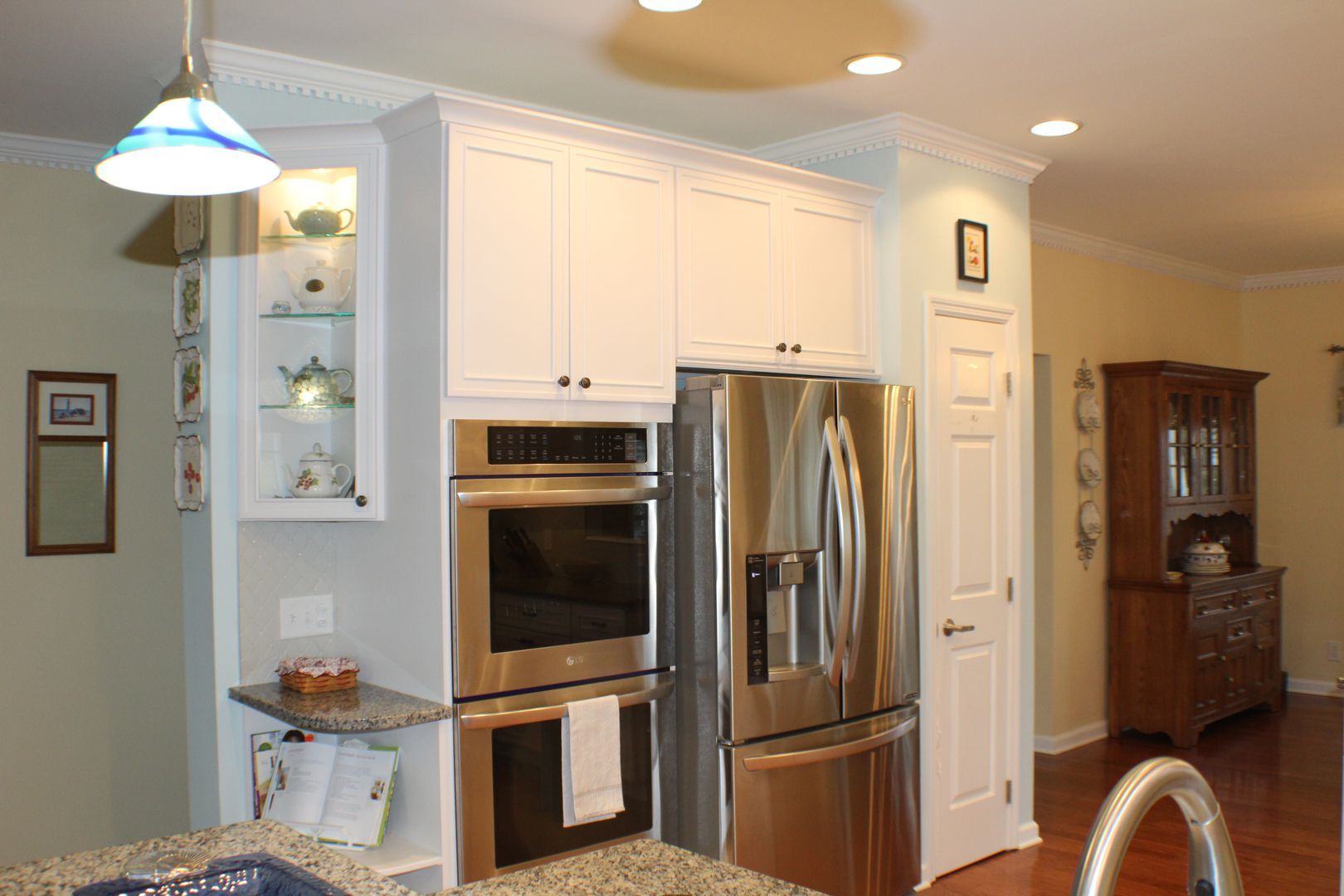 Modern kitchen with white cabinets, stainless steel refrigerator, built-in oven, and hanging light fixtures