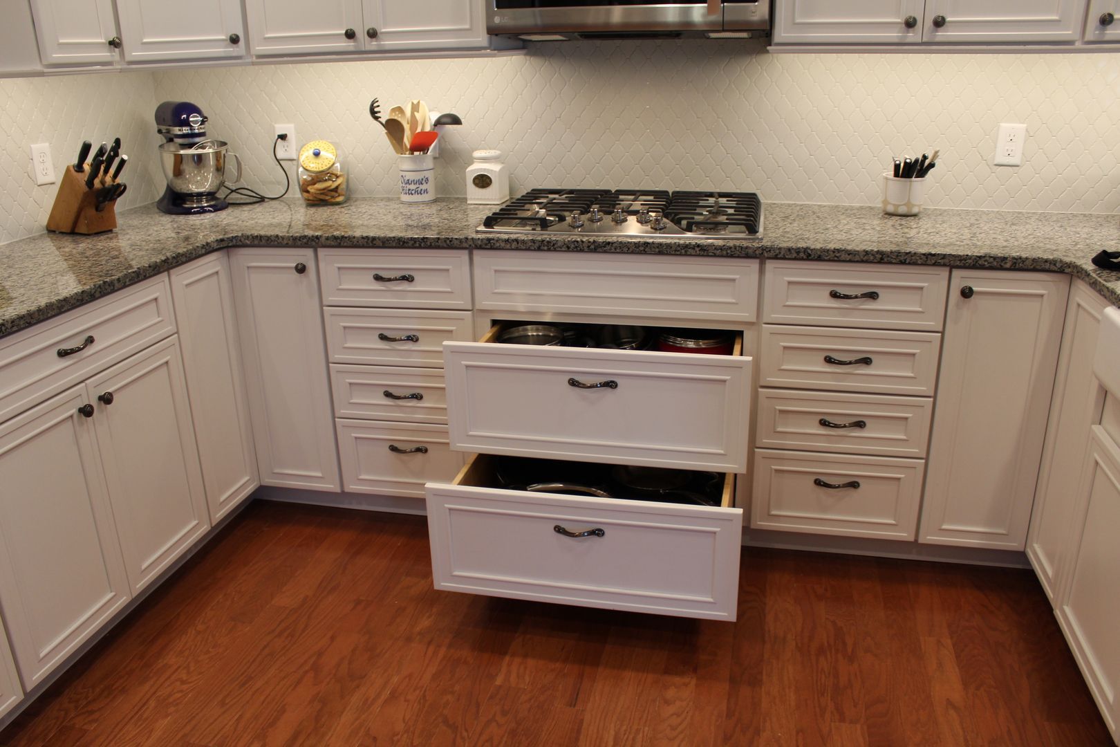 Modern kitchen with white cabinets, wood floor, granite countertop, and stove centered between drawers and appliances