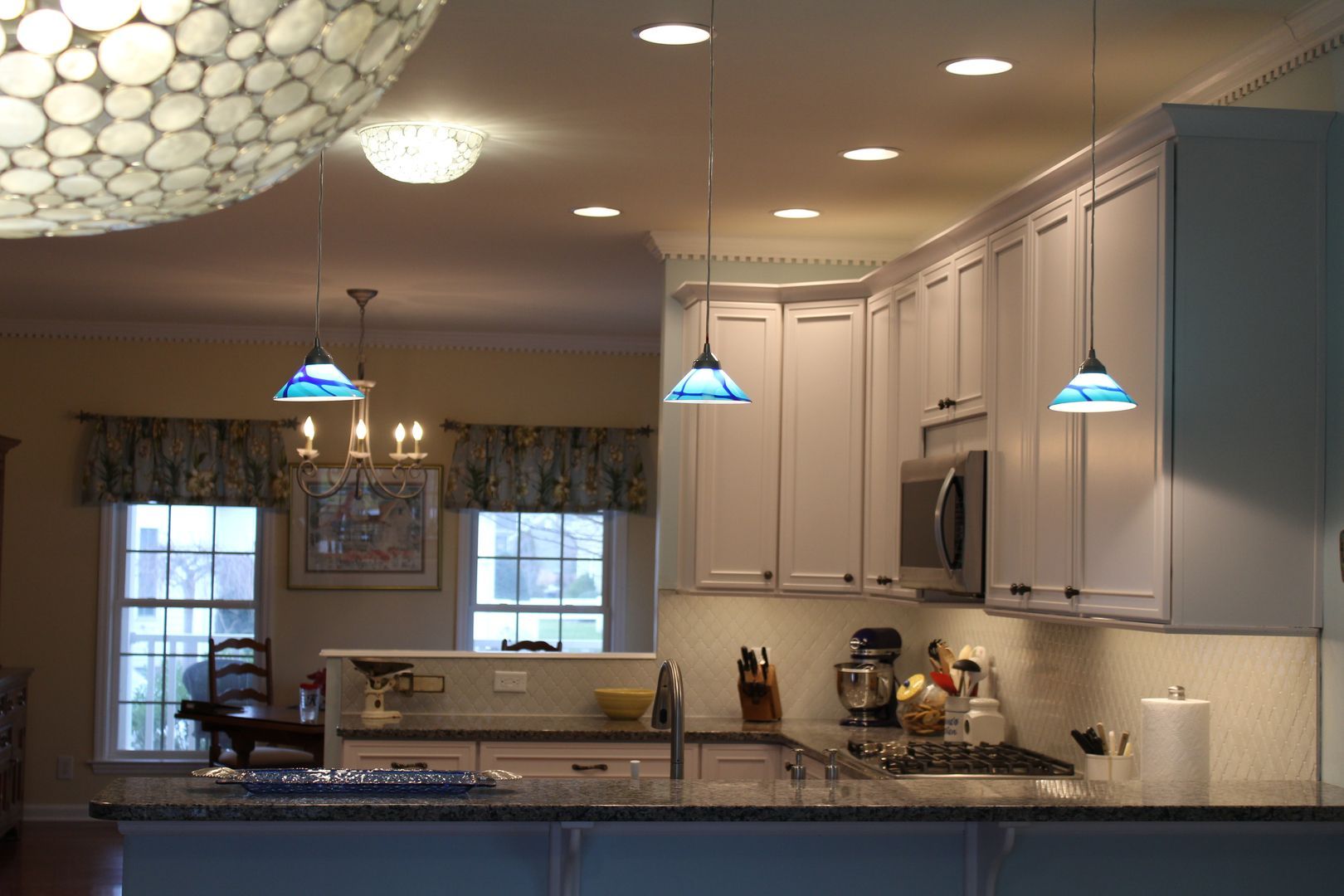 Modern kitchen with gray cabinets, blue pendant lights, and a granite island in warm recessed lighting
